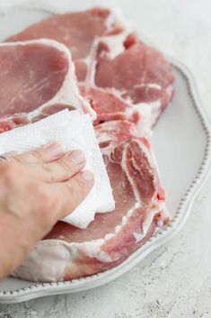 a person wiping down raw meat on a plate with a cloth in their left hand