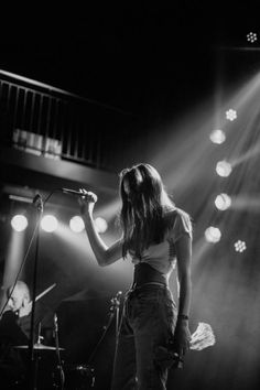 a woman standing in front of a microphone on top of a stage with lights behind her