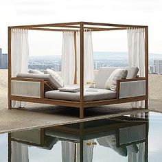 a canopy bed sitting on top of a pool next to a tall building with white curtains