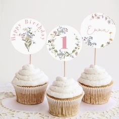 three cupcakes with white frosting and floral decorations