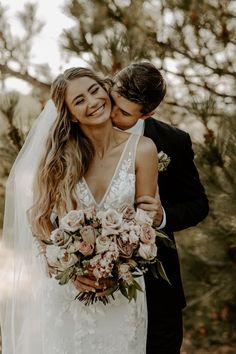 a bride and groom embracing each other in front of trees