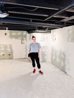 a woman standing in the middle of an unfinished room with white walls and black ceiling