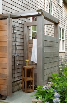 an outdoor shower in front of a house with wooden sidings and doors open to the outside