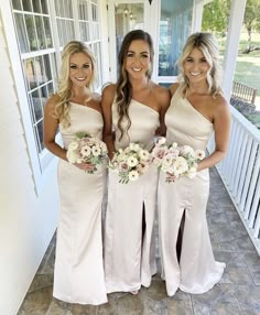 three bridesmaids in white dresses standing on the porch with bouquets and flowers