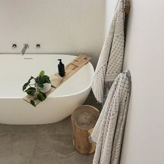 a white bath tub sitting next to a wooden basket filled with plants and towels on top of it