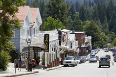 cars are parked on the street in front of shops and buildings with mountains in the background