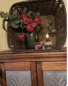 a basket filled with flowers sitting on top of a wooden dresser next to a candle