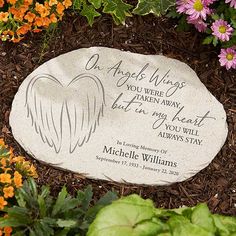 a memorial stone with an angel wings on it surrounded by flowers and plants in the background