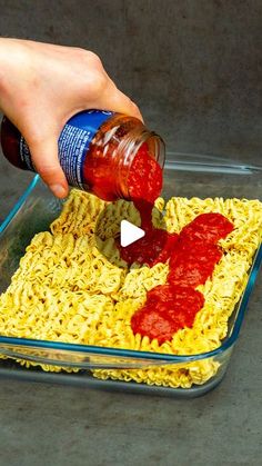 someone is adding ketchup to some noodles in a glass dish on the ground