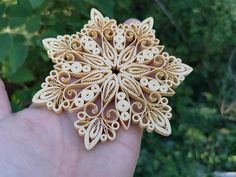 a hand holding a wooden brooch with intricate designs