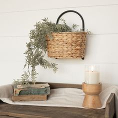 a basket hanging on the wall next to a candle and some books with an olive branch in it