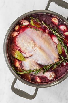 a raw chicken in a pot with herbs and spices on the side, ready to be cooked