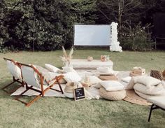 an outdoor movie set up in the grass with chairs and pillows on it, next to a screen