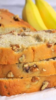 three slices of banana bread with walnuts on top and two bananas in the background