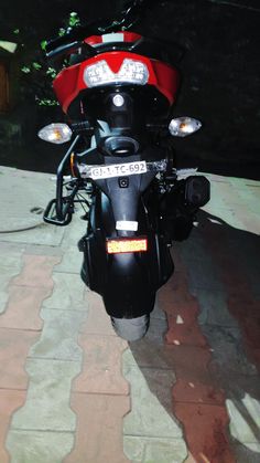 a red and black motorcycle parked on top of a brick walkway next to trees at night