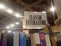 there is a sign that says classic literature hanging from the ceiling in front of bookshelves