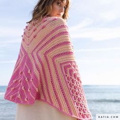 a woman standing on the beach wearing a pink crocheted shawl