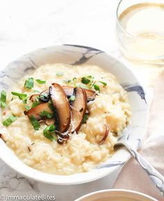 a white bowl filled with rice and mushrooms next to a glass of milk on a marble table