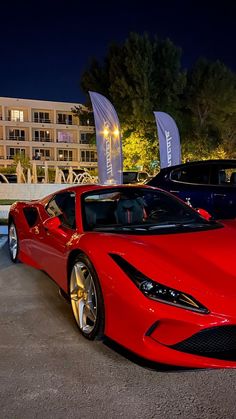 two red sports cars parked next to each other in front of a building at night