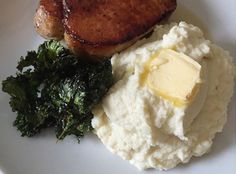 a white plate topped with meat and mashed potatoes next to green leafy greens