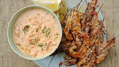 grilled shrimp and dipping sauce on a plate with lemon wedges, as well as a bowl of dip