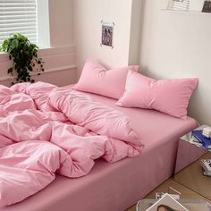 a bed with pink sheets and pillows in a room next to a plant on the floor