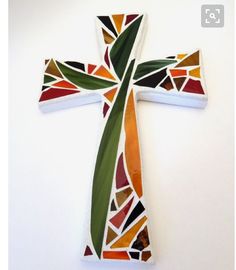 a cross made out of stained glass on a white wall with an orange and green design