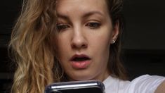 a woman holding a cell phone in her right hand and making a surprised face while looking at the screen