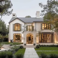 a large white house with lots of windows and plants on the front lawn, surrounded by greenery