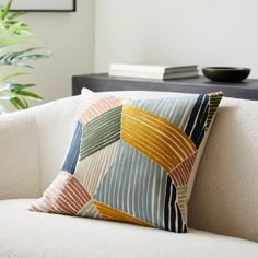 a white couch with a multicolored pillow on it next to a potted plant