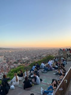 many people are sitting on the edge of a high building and enjoying the city view