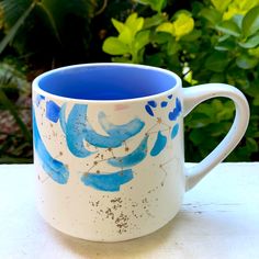 a blue and white coffee cup sitting on top of a table next to some bushes