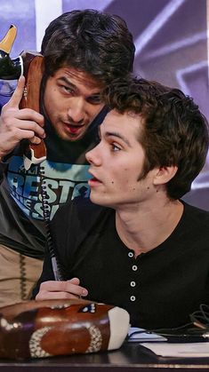 two young men sitting at a table and one is holding an object in his hand