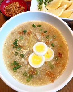 a bowl of soup with two boiled eggs in it and some other food on the side