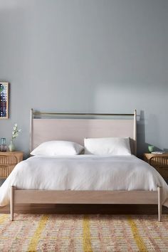 a bed with white linens and pillows in a gray room next to two nightstands