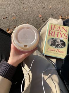 a person holding a coffee cup in their left hand and a book on the ground