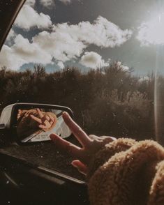 someone is holding their hand out the window of a car as they look at clouds in the sky