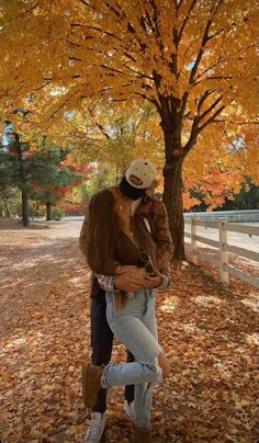 a man and woman kissing in front of a tree with autumn leaves on the ground