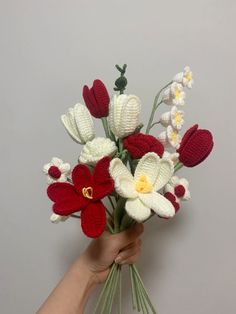 a hand holding a bouquet of crocheted flowers with red and white blooms in it