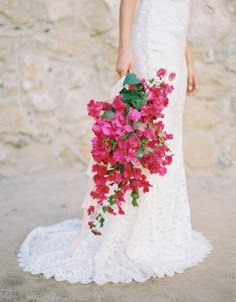 a woman in a white wedding dress holding a bouquet of pink flowers on her shoulder