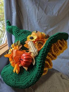 a crocheted green hat with flowers and leaves on the inside sits in front of a window