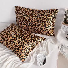 two pillows with leopard print on them sitting on a bed next to magazines and flowers