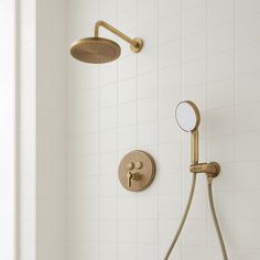 a shower head and hand shower in a white tiled bathroom with gold faucet