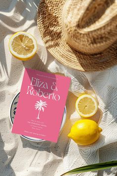 a pink book sitting on top of a table next to lemons and a straw hat