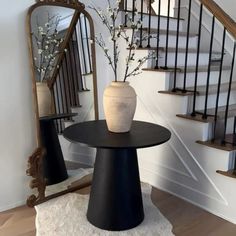 a vase sitting on top of a table in front of a mirror next to a stair case