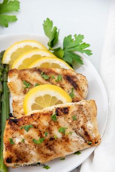 grilled fish with asparagus and lemon slices on a white plate next to parsley