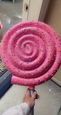 a person holding a giant pink object with sprinkles on it