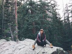 a woman sitting on top of a large rock in the woods