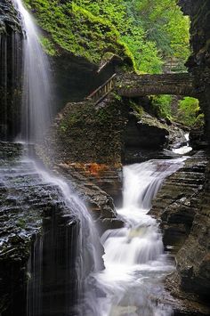 a waterfall with a bridge over it in the woods