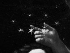 a black and white photo with stars in the sky above it, as well as a hand reaching for something